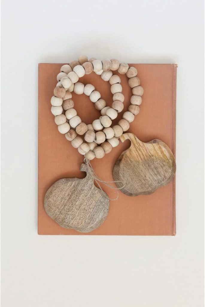 A beaded wooden necklace with two large, flat pendants rests on top of a closed, brown hardcover book against a white background.
