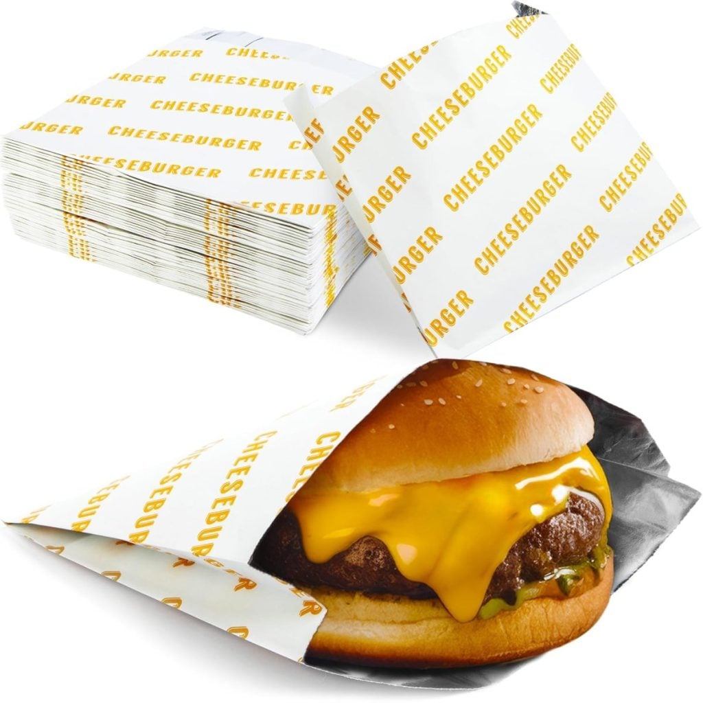 A cheeseburger wrapped in branded paper sits in front of a stack of identical yellow-and-white "CHEESEBURGER" wrappers.