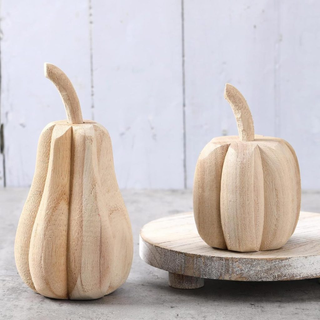 Two carved wooden gourds, one resembling a pear and the other a pumpkin, displayed on a round wooden board against a light rustic background.