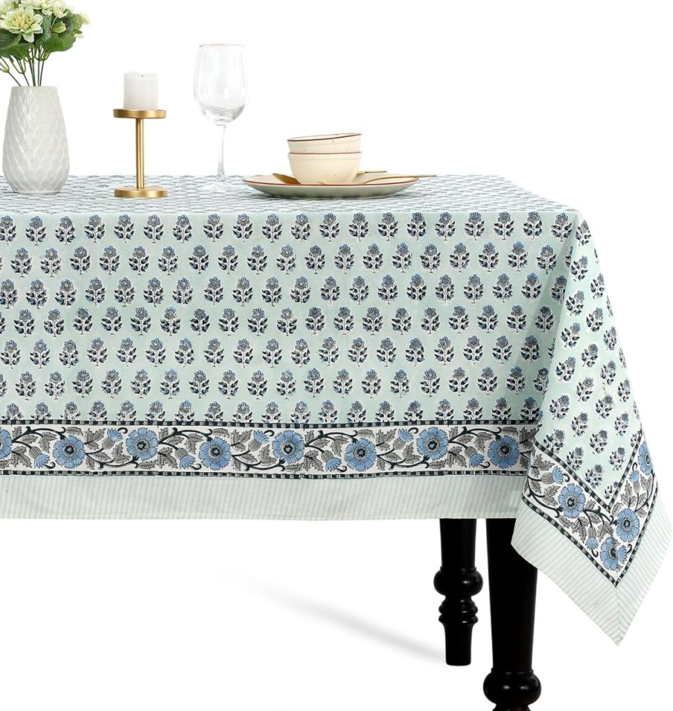A table with a blue and white floral patterned tablecloth, set with plates, bowls, a wine glass, a candle holder, and a vase with flowers.