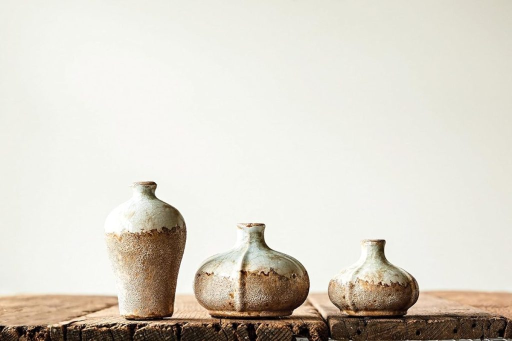 Three small ceramic vases with rustic brown and white glaze are displayed on a wooden surface against a plain, light background.