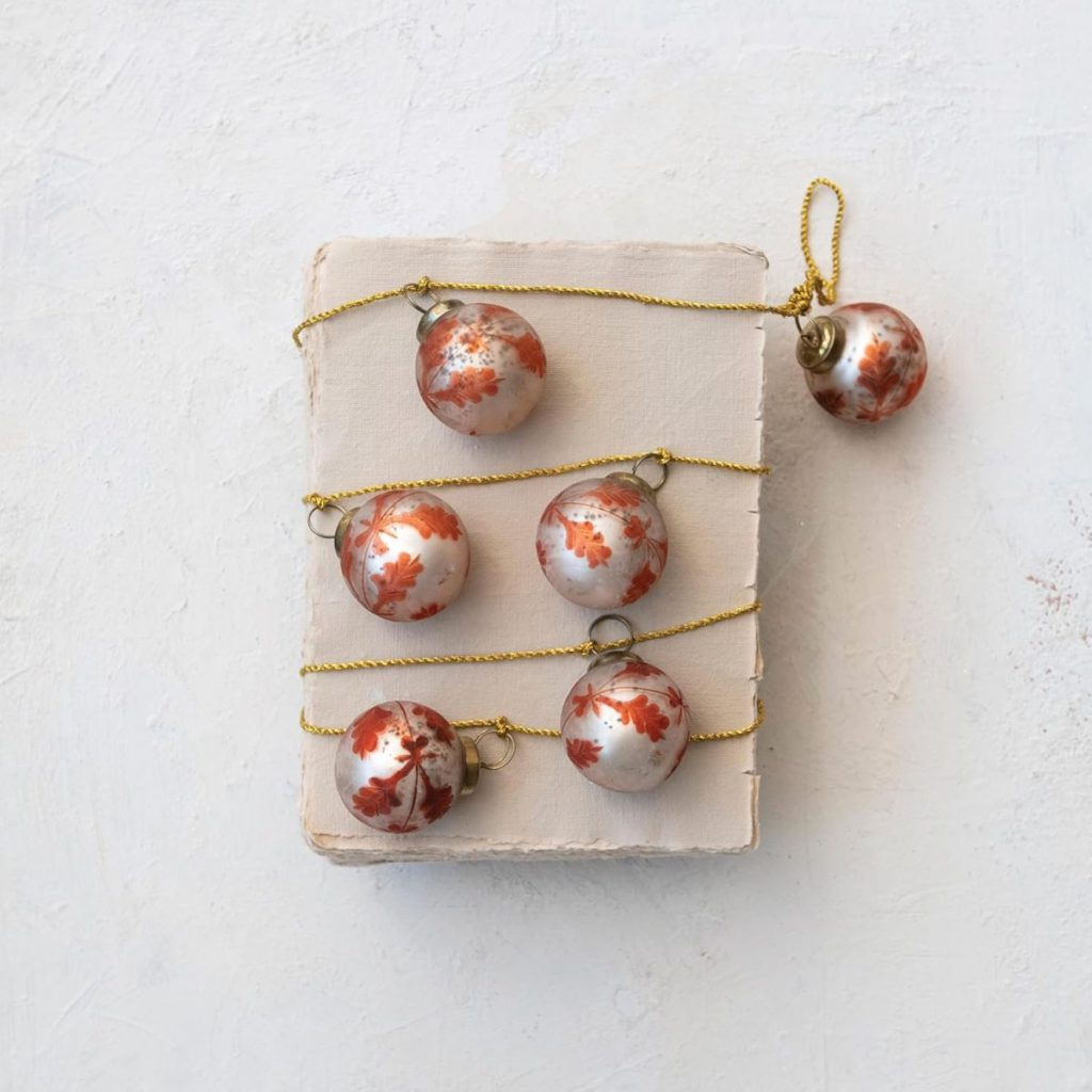 Five red and white marbled Christmas ornaments are arranged in rows on a textured white surface, connected by a gold string.