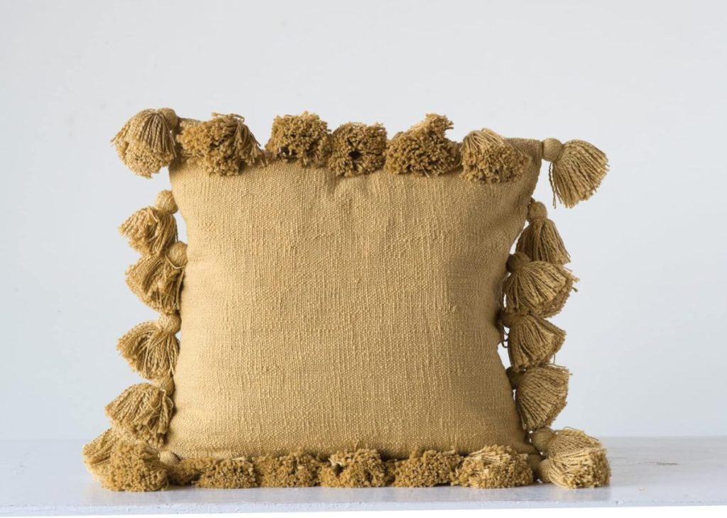 Square mustard-yellow throw pillow with textured tassels along all four edges, set against a plain white background.