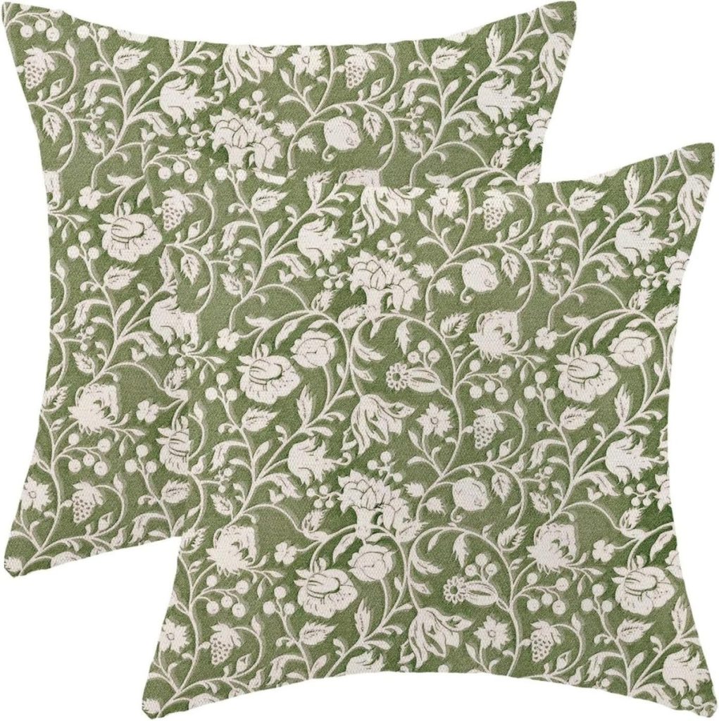 Two square green cushions with a white floral and vine pattern overlap each other against a plain background.