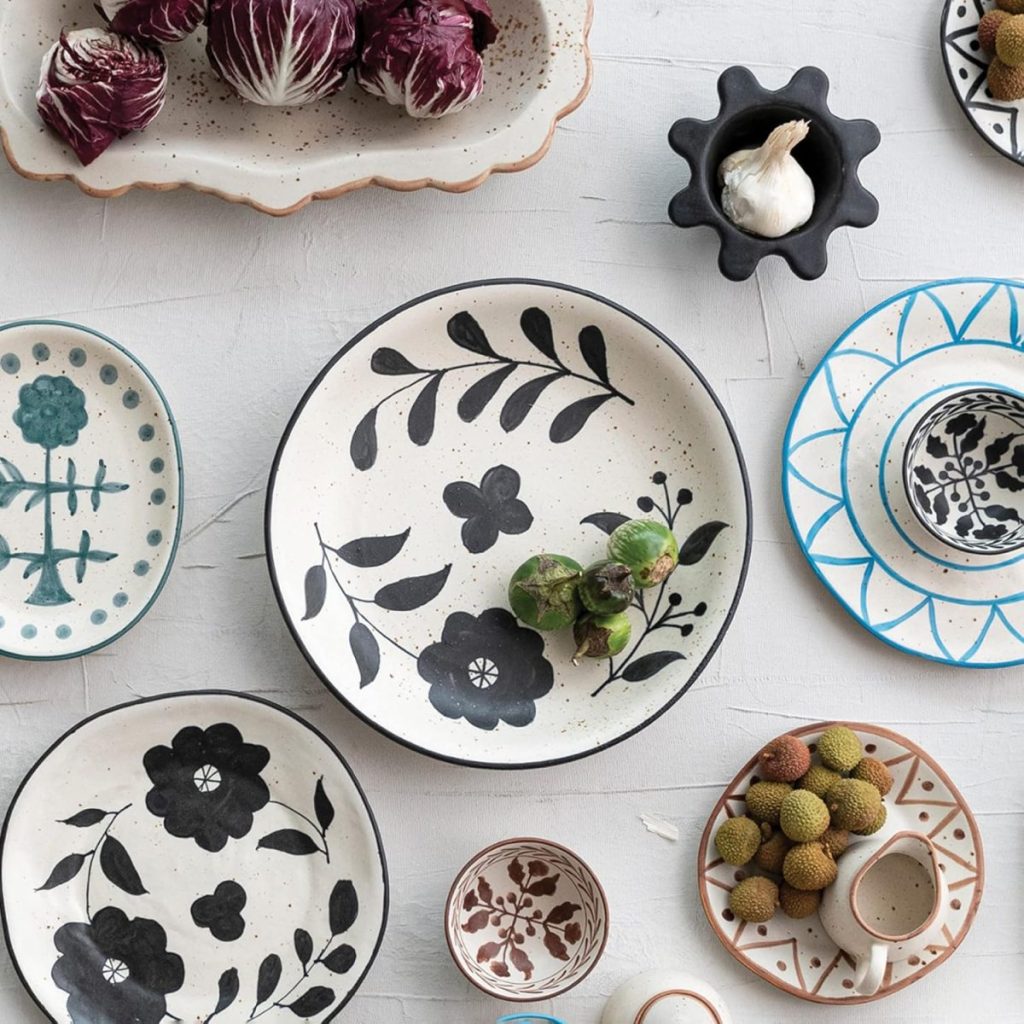 Assorted ceramic plates and bowls with floral patterns arranged on a white surface, some holding vegetables, lychees, and garlic.
