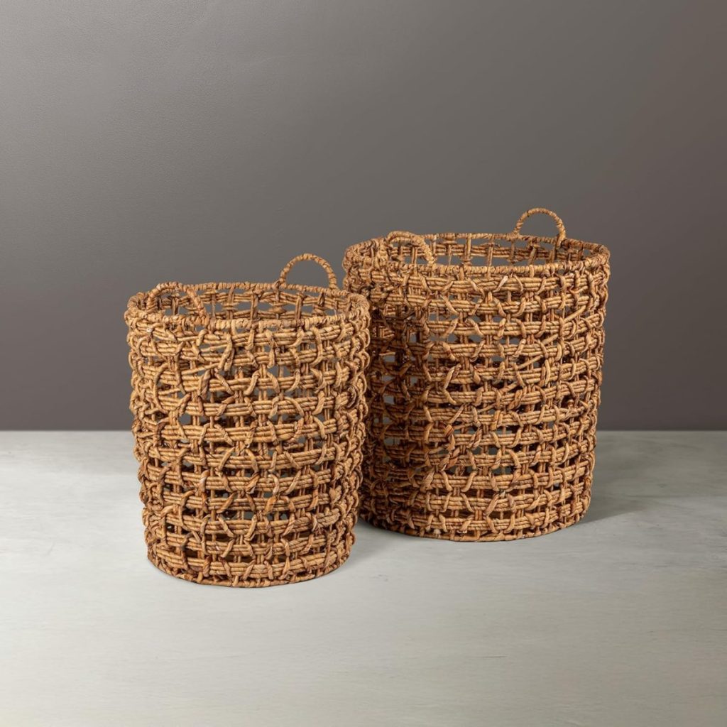 Two cylindrical woven baskets with handles are placed side by side on a light-colored surface against a gray background.