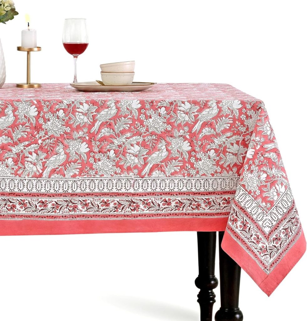 A red and white floral-patterned tablecloth covers a rectangular table set with dishes, a candle, and a glass of red wine.