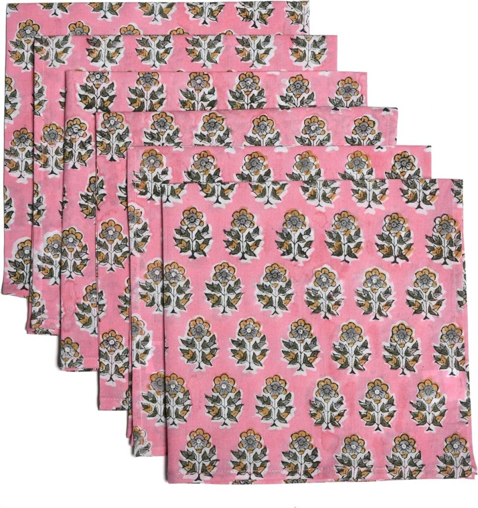 Six folded pink cloth napkins with a repeating floral print pattern in yellow, white, and green.