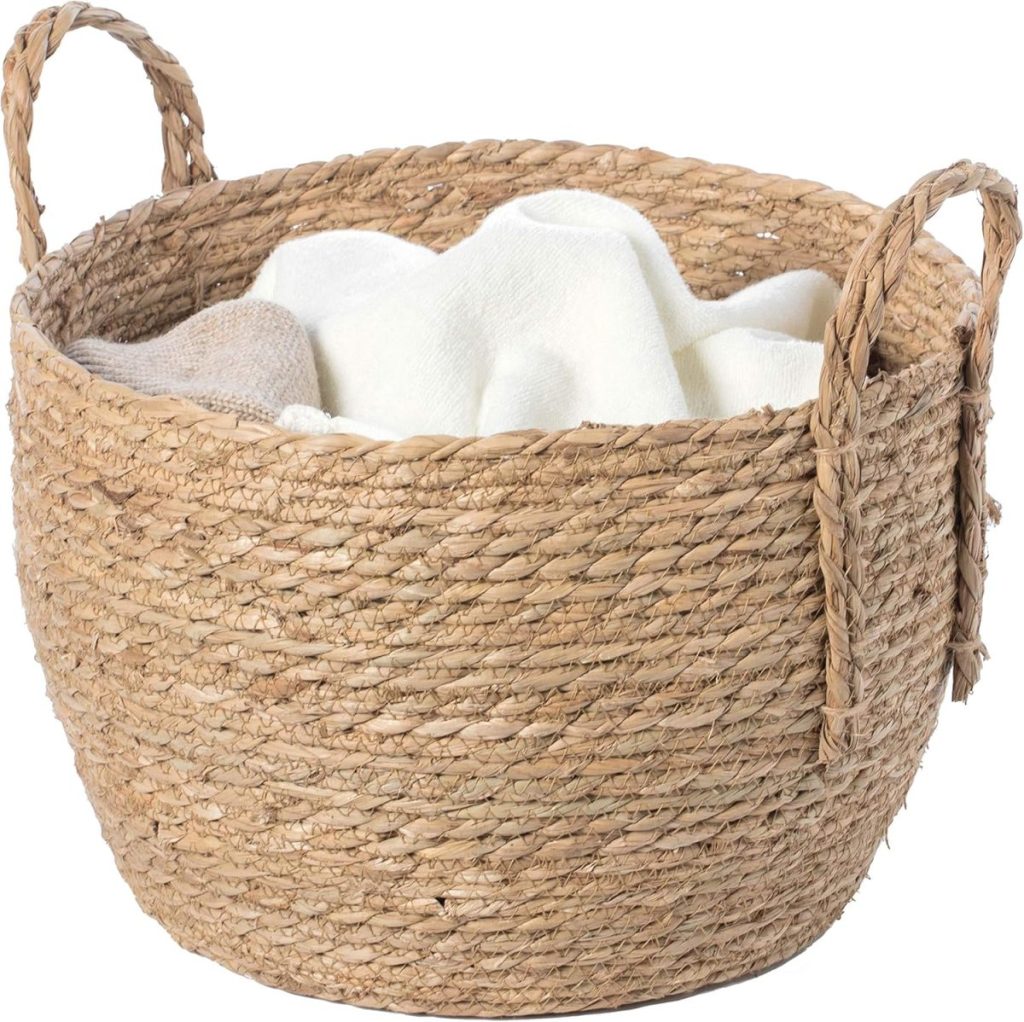 A woven wicker basket with two handles, filled with beige and white folded towels or cloths.