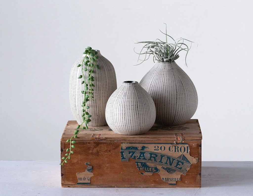 Three white vases with dotted patterns, two holding trailing plants, placed on a vintage wooden crate with blue lettering.