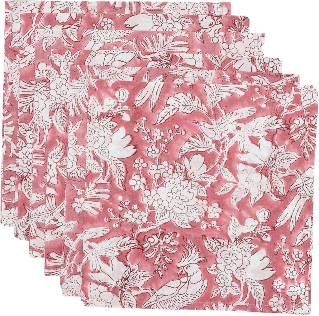 A set of four pink cloth napkins featuring a white floral and bird pattern, arranged in a stacked, overlapping layout.