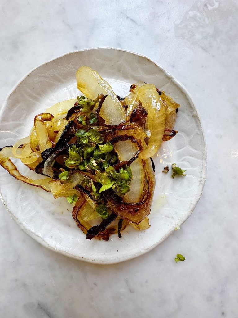 A white plate with caramelized onion slices topped with chopped green herbs, set on a marble surface.