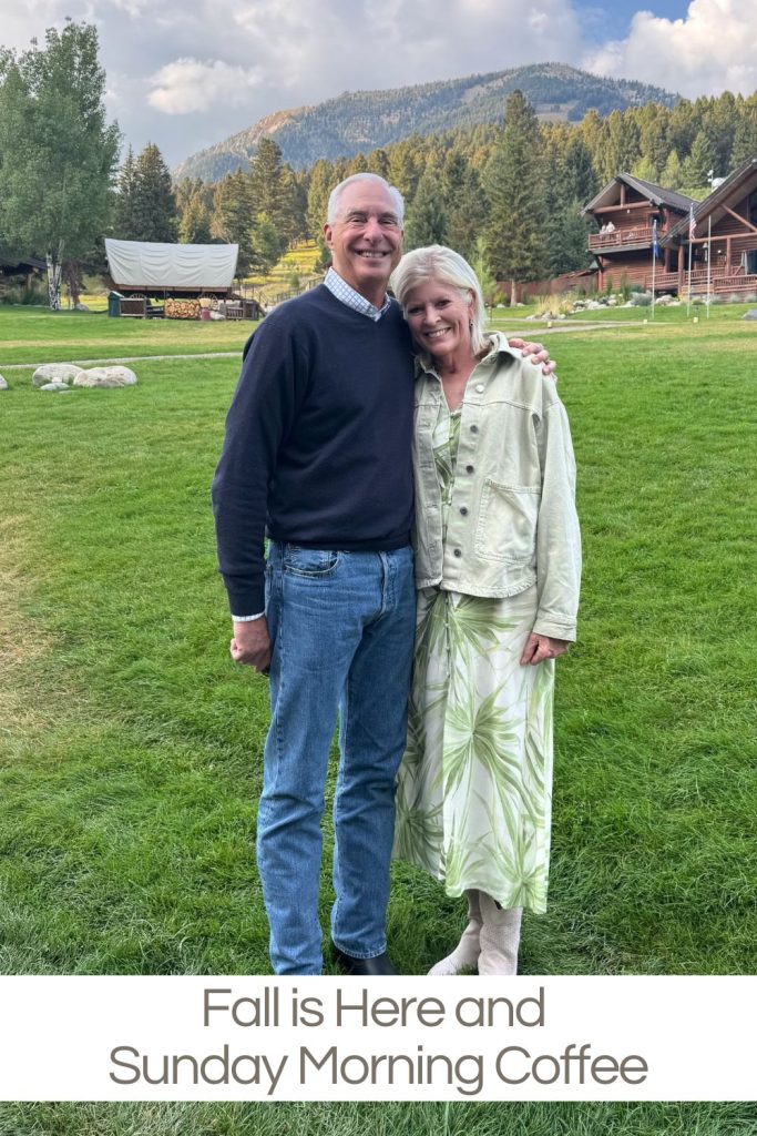 A smiling couple stands close together on a grassy lawn with cabins, trees, and mountains in the background. The caption reads, "Fall is Here and Sunday Morning Coffee.