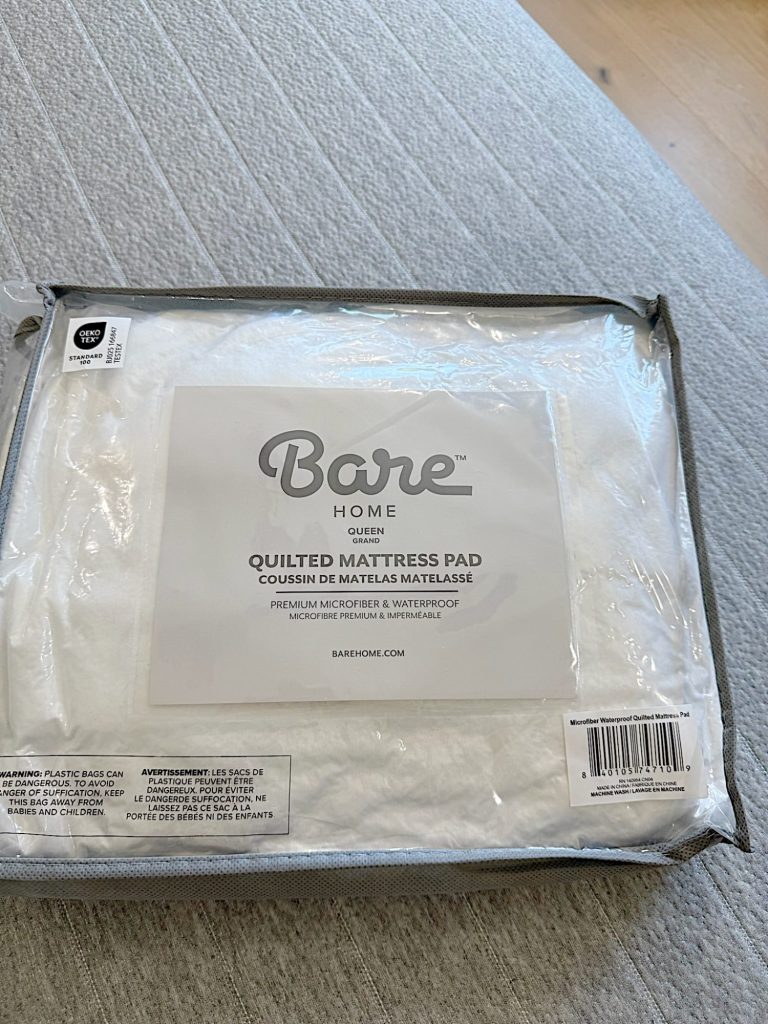 A packaged Bare Home queen-size quilted mattress pad labeled as premium microfiber and waterproof, placed on a light-colored surface.