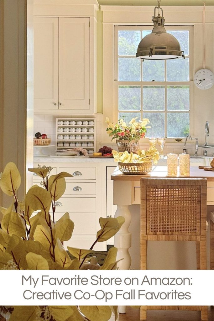 Bright, cozy kitchen with wicker chairs, white cabinets, a basket of fruit on the counter, and fall-themed decor. Text overlay reads: "My Favorite Store on Amazon: Creative Co-Op Fall Favorites.