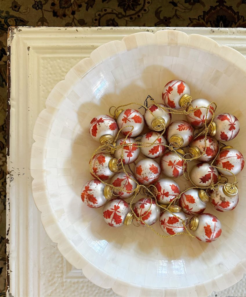 A white bowl filled with small white ornaments decorated with red maple leaves, sitting on a textured white surface.