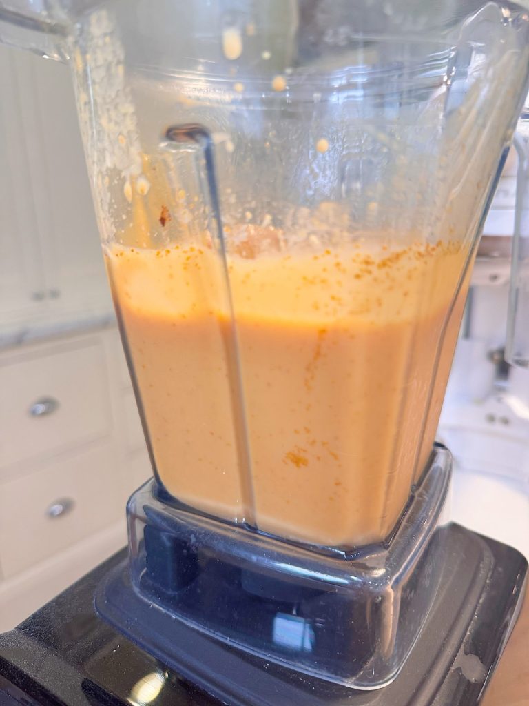A blender filled with a thick, orange liquid mixture is sitting on a kitchen counter.