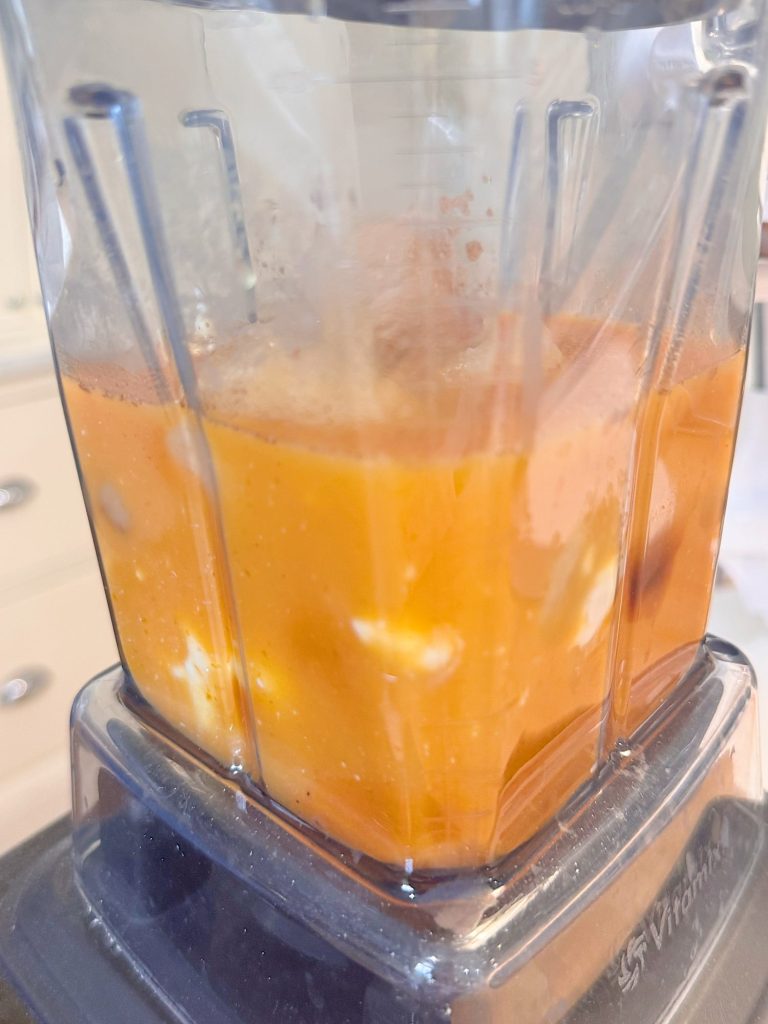 A close-up of a blender containing chopped orange fruits and ice being blended into a liquid.