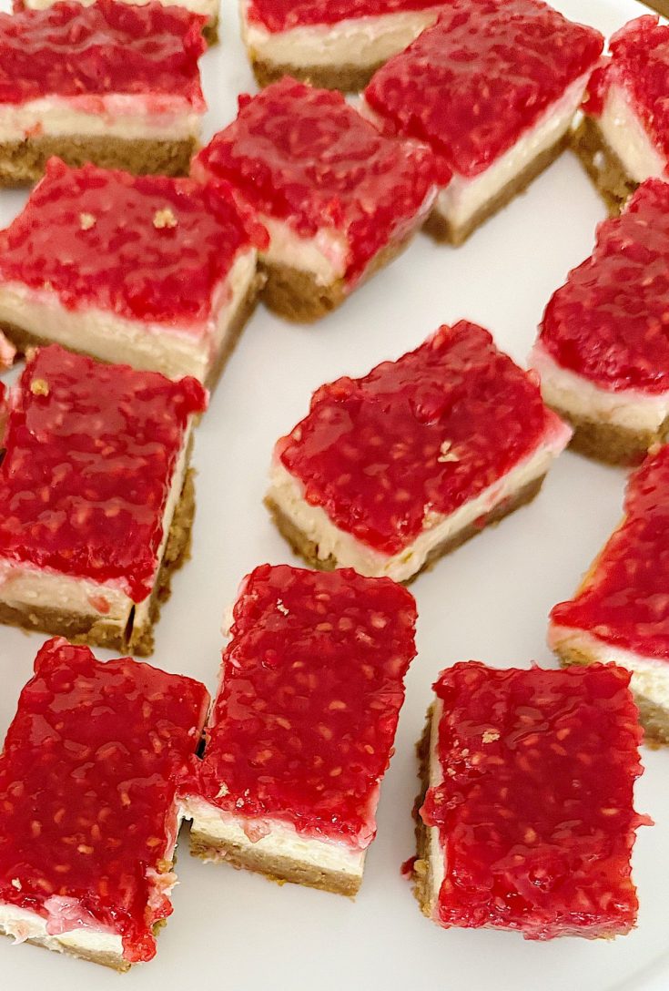 Several rectangular raspberry cheesecake bars with a graham cracker crust are arranged on a white surface.