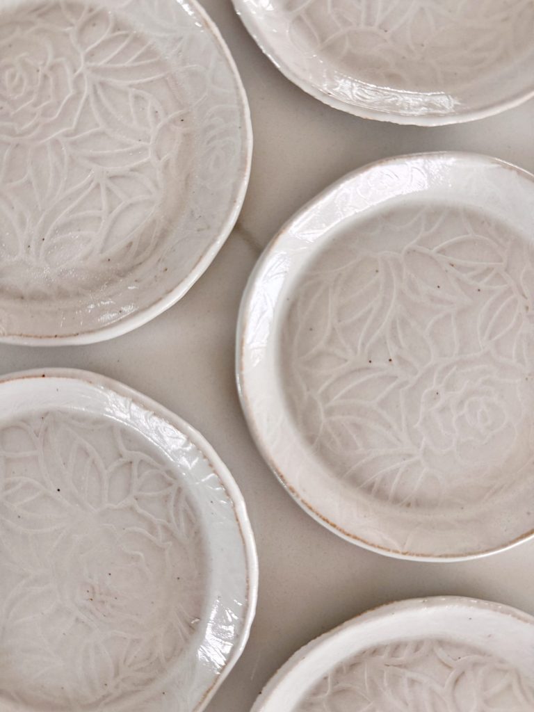 Six white ceramic plates with embossed floral patterns arranged closely on a light surface.