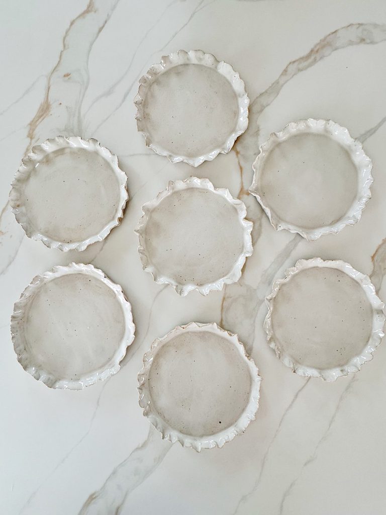 Seven round ceramic plates with uneven, ruffled edges are arranged on a white marble surface.