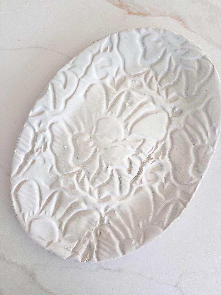 An oval white ceramic plate with an embossed floral pattern on its surface, placed on a light-colored marble countertop.