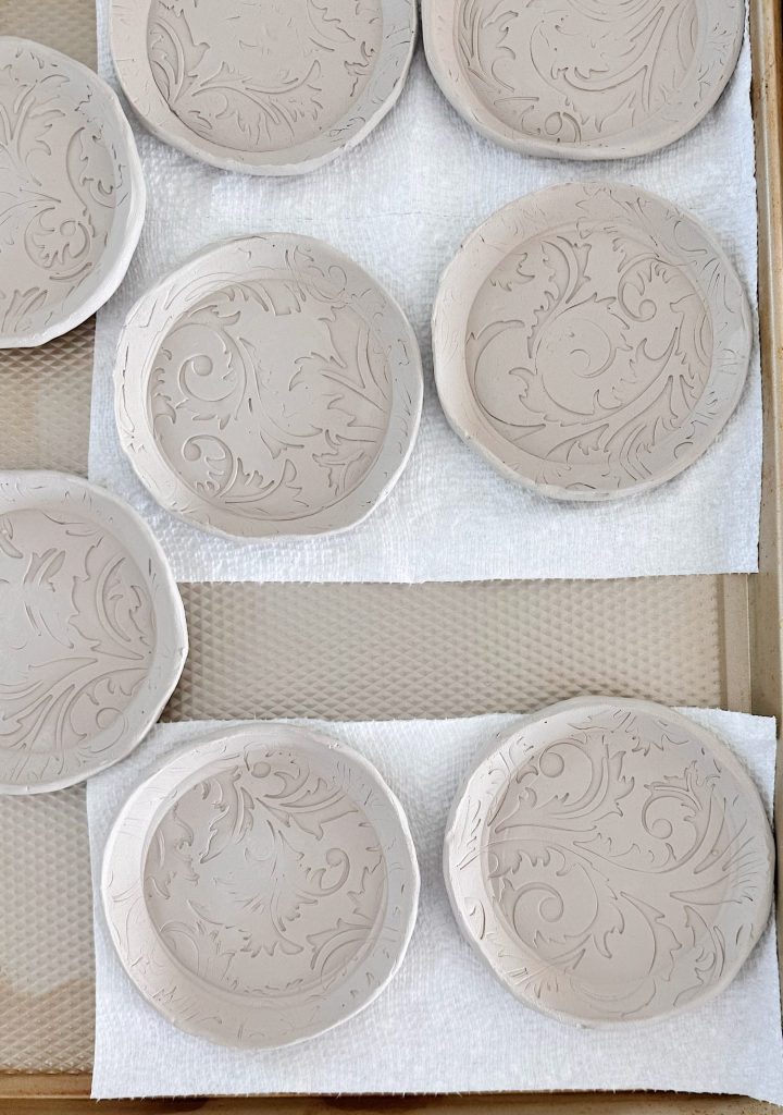 Round clay coasters with embossed floral patterns are drying on paper towels arranged on a tray.