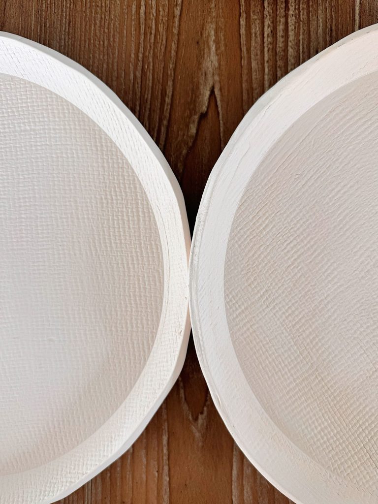 Two white textured plates are placed closely side by side on a wooden surface, with only parts of each plate visible.