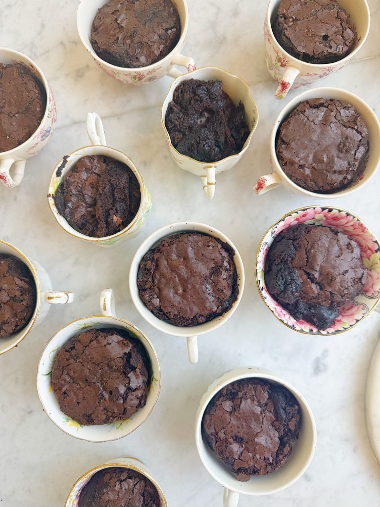 Several teacups filled with baked chocolate cake, arranged on a white marble surface.