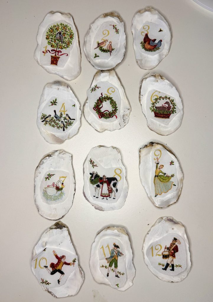 Twelve oyster shells painted with images and numbers representing the Twelve Days of Christmas, each with a different festive illustration.