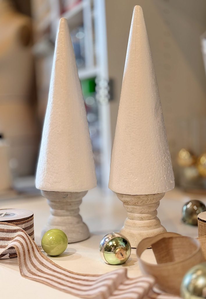 Two white cone-shaped objects on stands are placed on a table, surrounded by striped ribbon rolls and shiny green and silver ornaments.