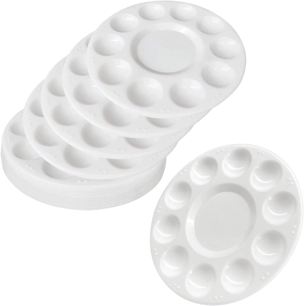 A stack of white plastic paint palettes, each with ten small wells surrounding a larger central well.