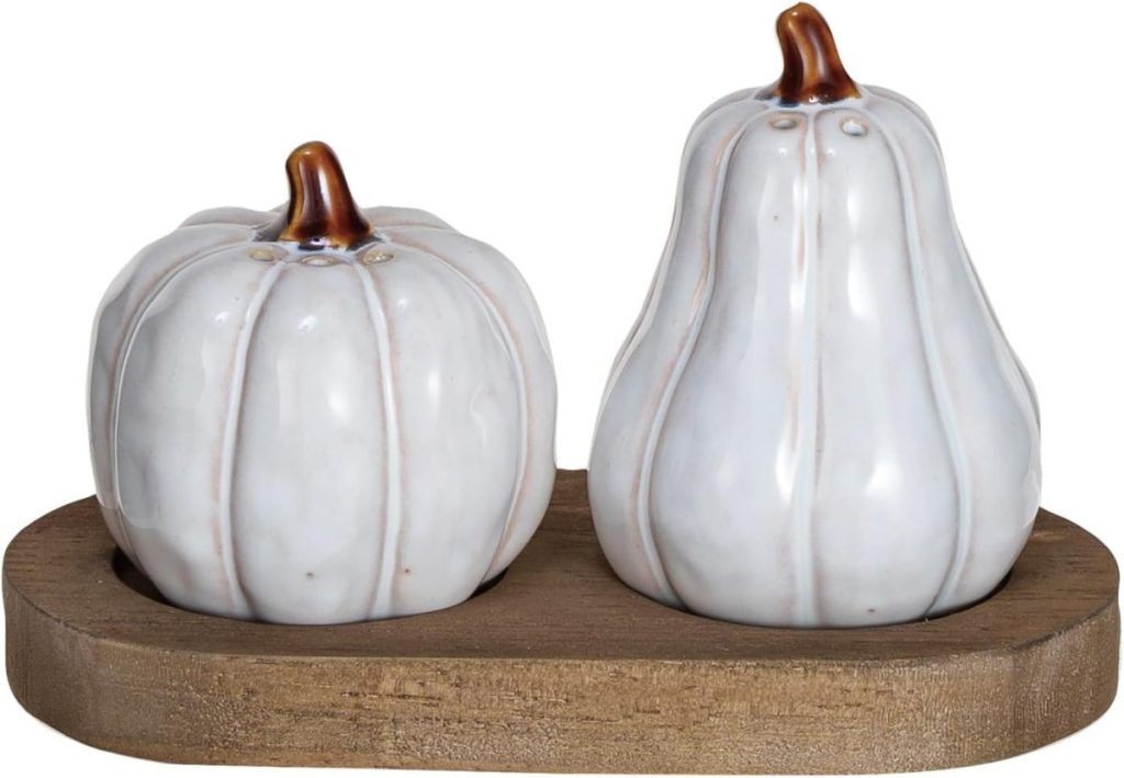 Two ceramic shakers shaped like a pumpkin and a gourd sit on a small wooden tray.