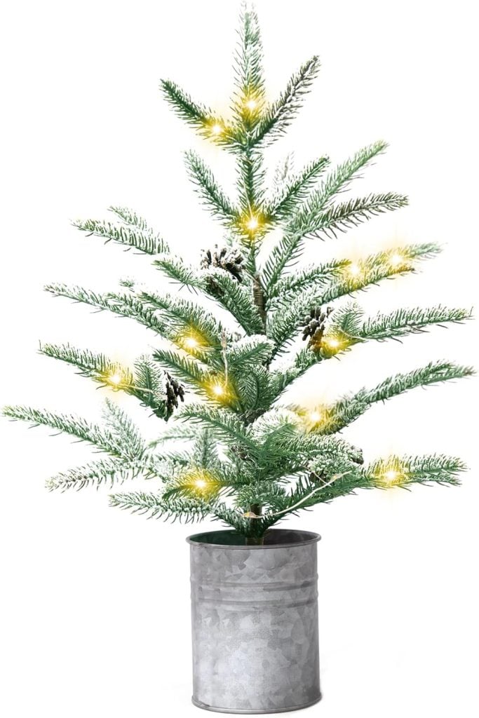 A small artificial Christmas tree with pine cones and yellow lights, placed in a metallic bucket-style pot, accented with festive gift tags for a charming holiday touch.