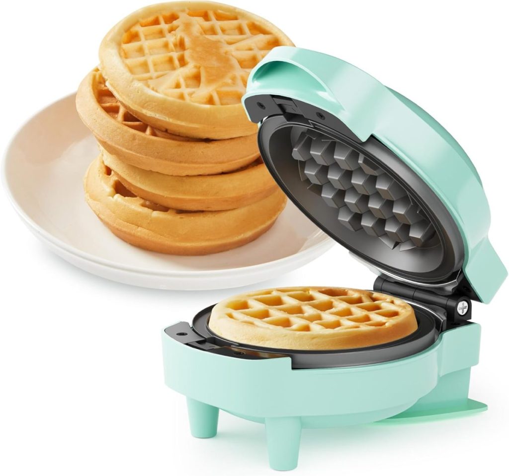 A small mint green waffle maker with a waffle inside sits open next to a plate stacked with four Porto-style waffles.