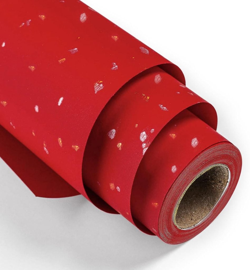 A close-up of a roll of red wrapping paper with scattered gold and silver specks, perfect for pairing with festive gift tags.