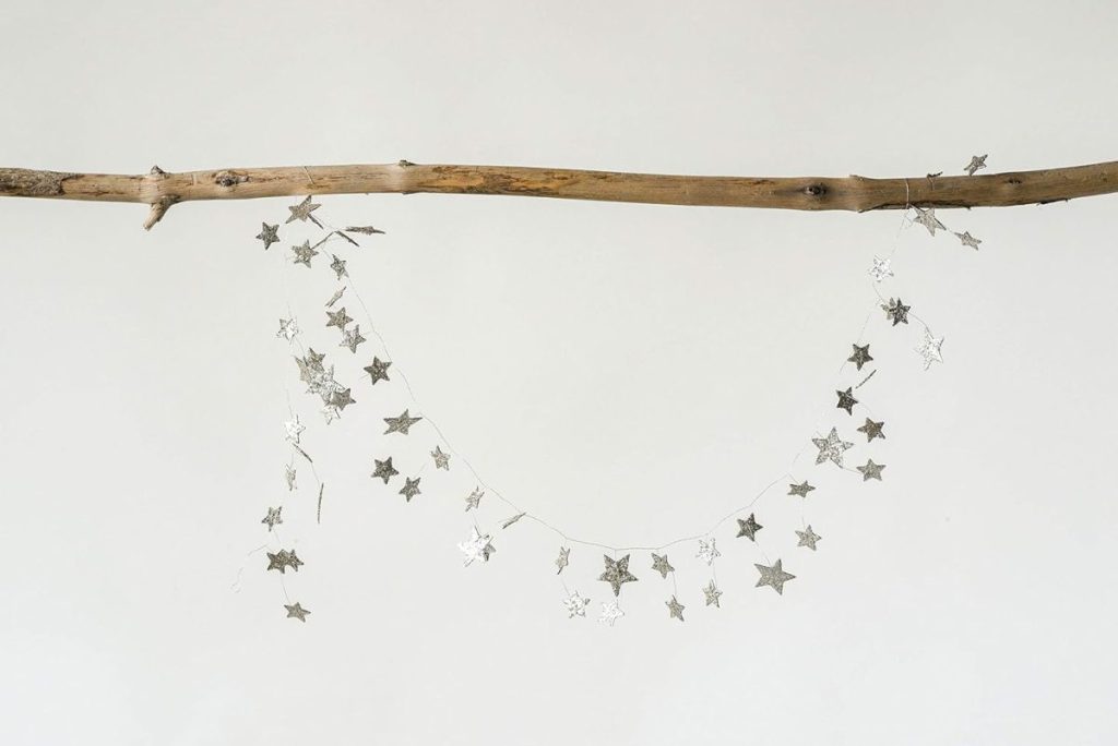 A thin branch is suspended horizontally against a plain background, with a string of metallic and air dry clay star-shaped ornaments draped across it.