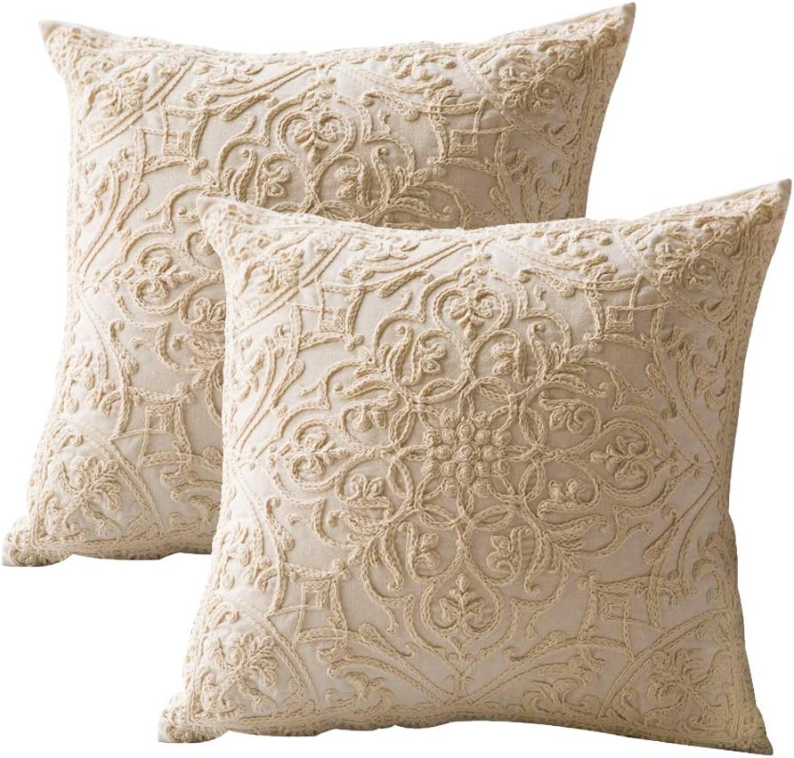 Two square decorative throw pillows with intricate cream-colored embroidered patterns on a light beige fabric background.