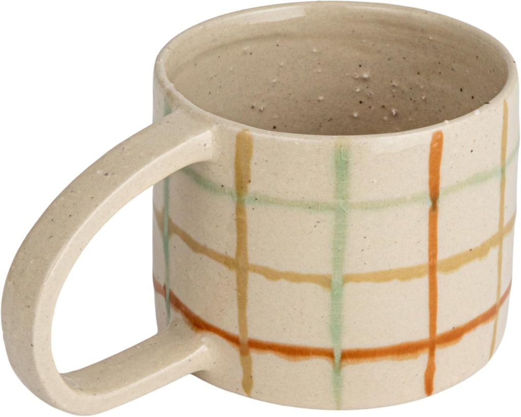 Beige ceramic mug with a large handle and a grid pattern in orange, yellow, and green lines on the exterior surface, inspired by Porto’s vibrant design aesthetic.