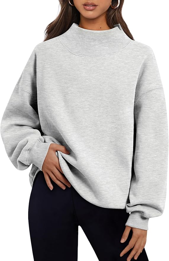 A woman wearing a light gray, long-sleeve, mock-neck sweatshirt and black pants, with one hand resting on her hip—perfect for scoring style during Amazon Prime Big Deal Days.