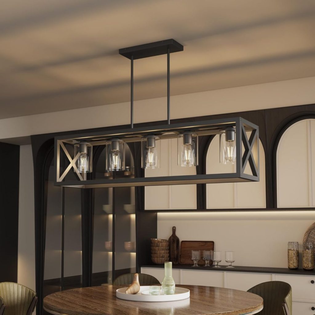Rectangular black metal chandelier with exposed bulbs hangs above a round wooden dining table in a modern kitchen with arched cabinets and warm lighting.