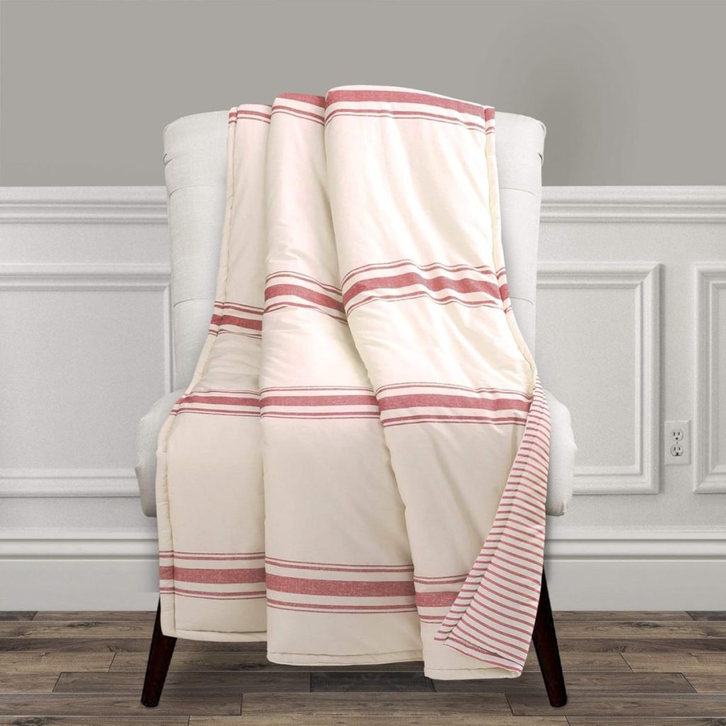 A white upholstered chair with a cream blanket featuring red stripes draped over it, set against a paneled wall and hardwood floor—perfect for cozying up during Amazon Prime Big Deal Days.