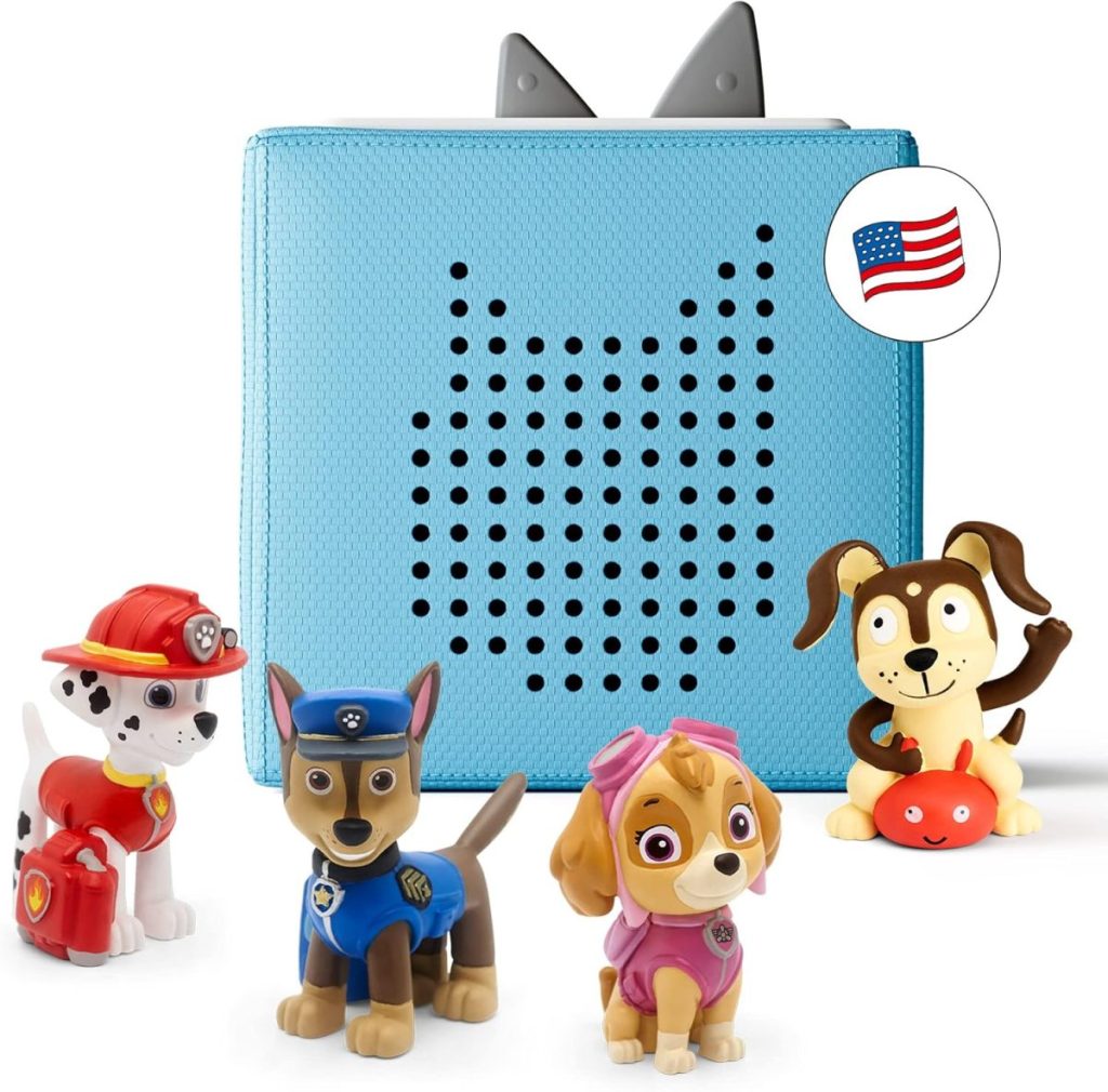 A blue kids' audio player with cat-shaped speakers and four Paw Patrol figurines, including a dog holding a red object. An American flag icon is shown in the corner—perfect for Amazon Prime Big Deal Days.