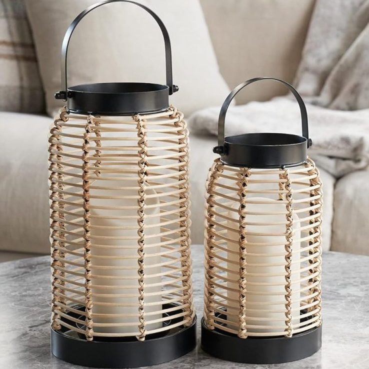 Two wicker lanterns with handles sit on a round marble coffee table in front of a beige sofa with neutral-colored pillows and a blanket, adding cozy outdoor fall decor to the inviting space.