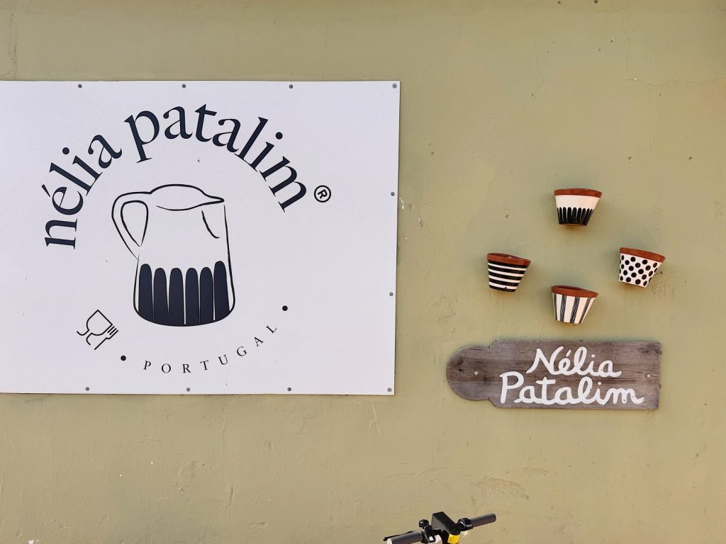 A sign reading “nélia patalim Portugal” next to four decorative pots and a wooden plaque with “Nélia Patalim” handwritten on it, all mounted on a light green wall.