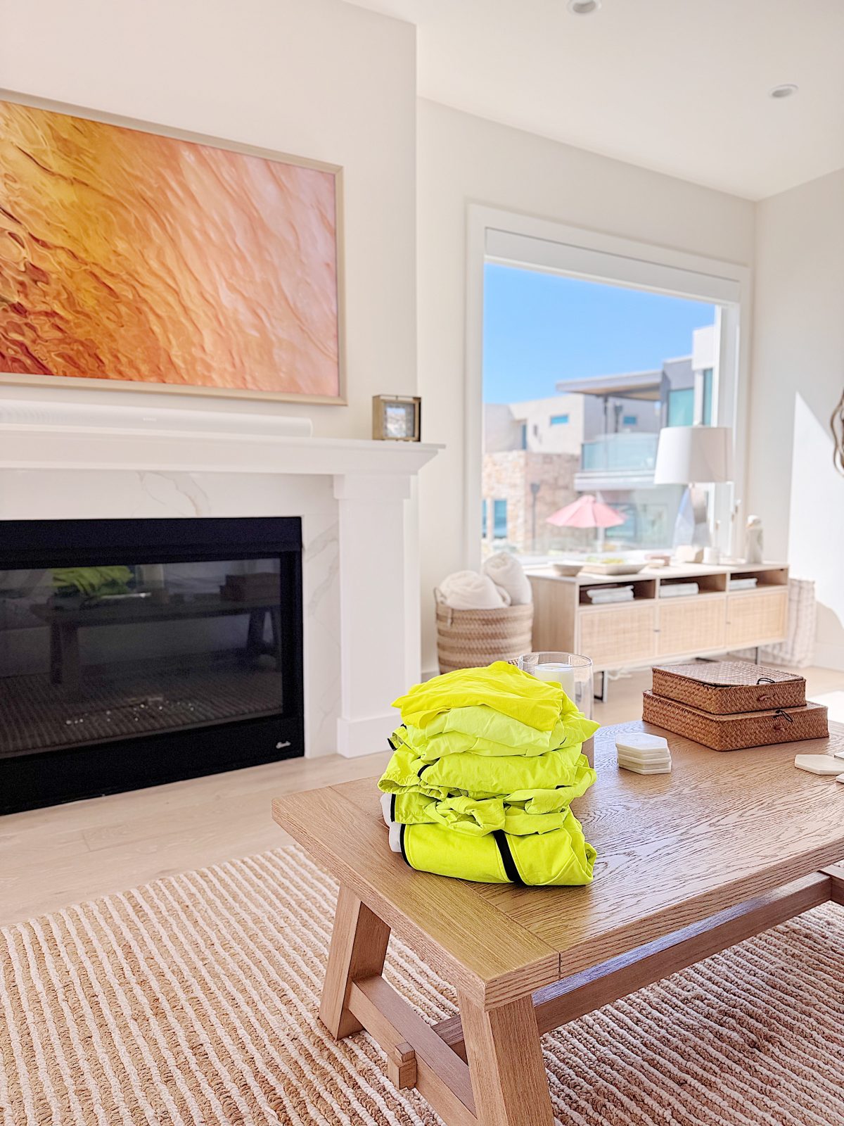 A stack of bright yellow life jackets sits on a wooden coffee table in a modern, sunlit living room in Portugal, complete with a fireplace and large window.