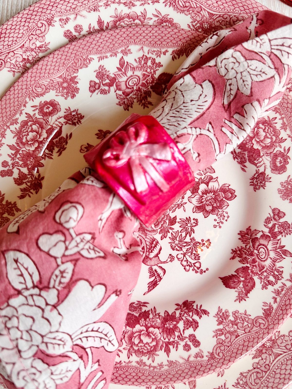 Pink and white floral napkin with a pink napkin ring placed on top of a pink and white floral patterned plate.