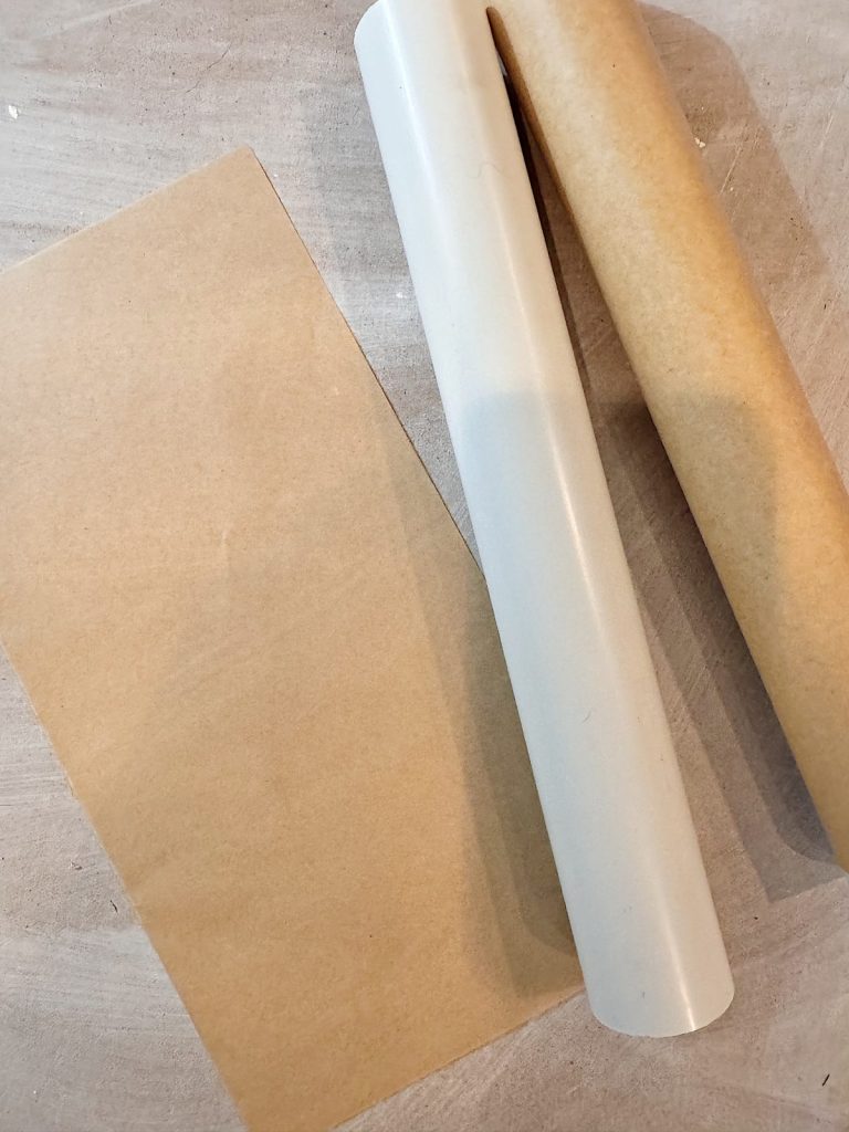 A roll of parchment paper, a plastic tube, and a rectangular sheet of parchment paper on a light-colored surface.