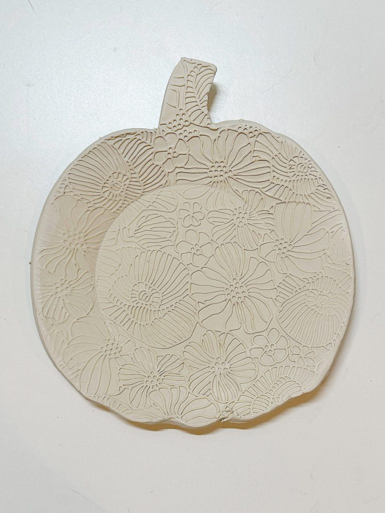 A flat, pumpkin-shaped clay dish with an embossed floral pattern, displayed on a plain white background.