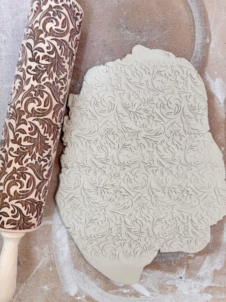 A patterned rolling pin next to a sheet of clay embossed with the same intricate floral design.